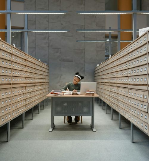 A girl studies among card catalogs in a library, focused on learning and research.